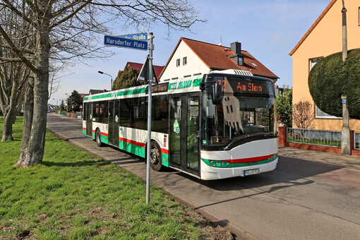 Ein grün-weiß-schwarzer Bus der Magdeburger Verkehrsbetriebe im vorortlichen Umfeld. Im Hintergrund sind mehrere Einfamilienhäuser zu sehen