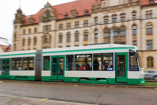Eine grün-weiße Straßenbahn der Magdeburger Verkehrsbetriebe fährt über den Breiten Weg. Im Hintergrund ist das Justizzentrum Eike von Repgow zu sehen.